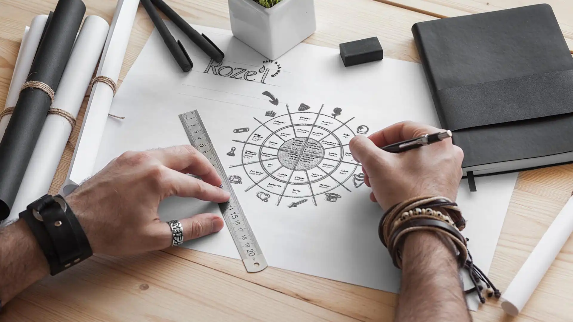 Deux mains travaillent sur un dessin circulaire complexe sur une table en bois avec des outils de dessin.