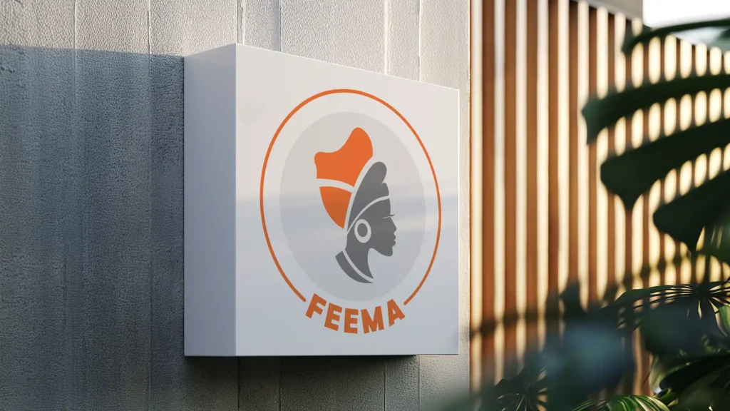 une enseigne blanche rectangulaire avec le logo "FEEMA" représentant un profil féminin stylisé en gris et orange, fixée sur un mur texturé gris avec des éléments décoratifs en bois et des feuilles de plante en arrière-plan.