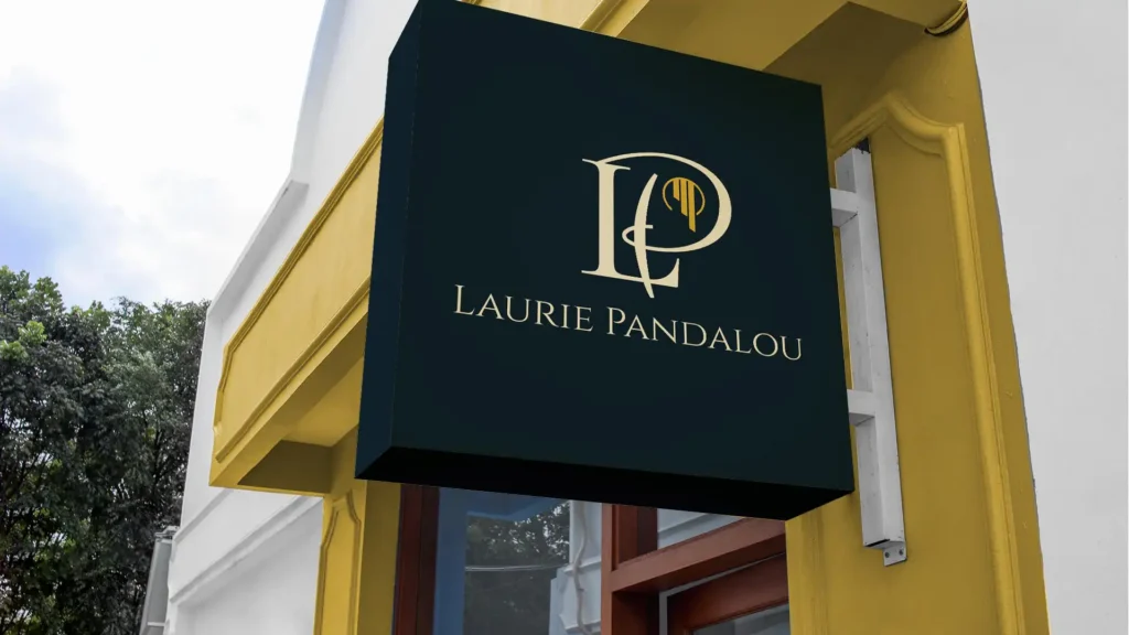 Enseigne noire rectangulaire avec le logo 'LP' doré et le texte 'LAURIE PANDALOU', suspendue à un bâtiment jaune avec une fenêtre.